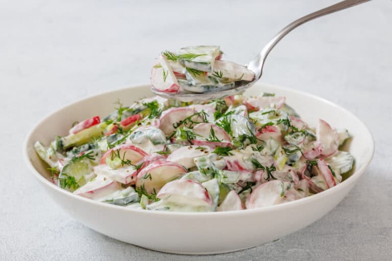 A bowl of creamy radish salad garnished with dill, with a spoon lifting a portion above the bowl.
