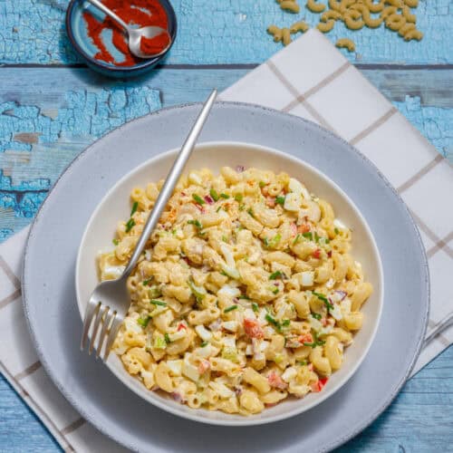 A bowl of Deviled Egg Pasta Salad with diced vegetables and herbs on a white plate.