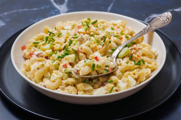 Deviled Egg Pasta Salad with diced vegetables, garnished with chives, on a white plate.
