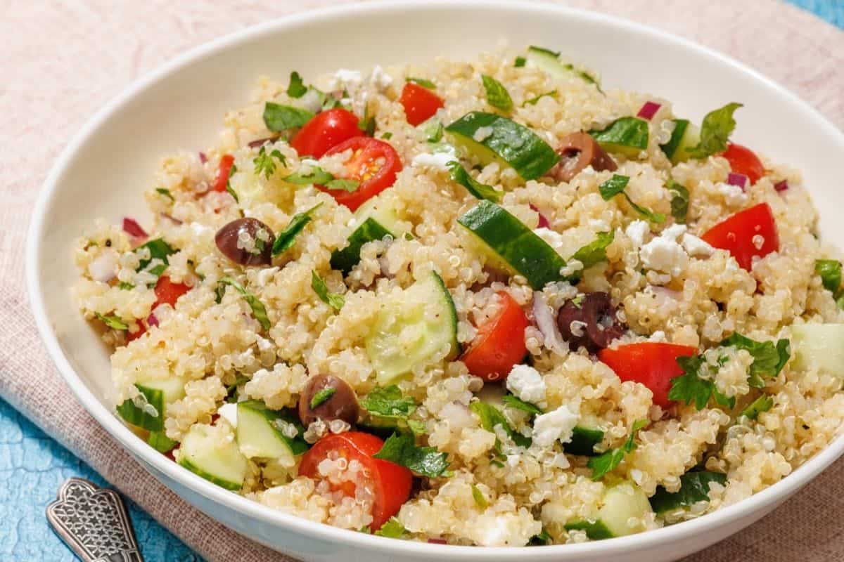 A white bowl of Mediterranean Quinoa Salad on a light blue tablecloth.