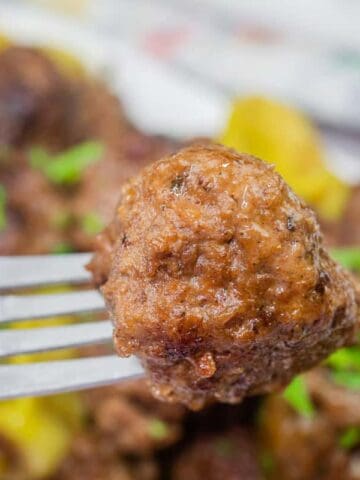 A close-up of a meatball on a fork, with more meatballs in the background.
