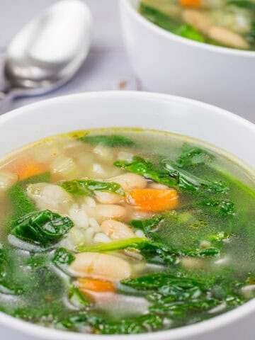 Bowl of Rice and White Bean Soup with spinach, carrots, and beans on a tiled surface.