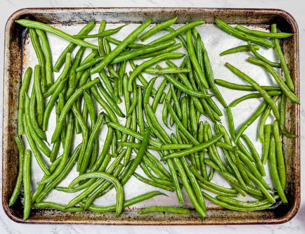 A baking tray with uncooked green beans spread out evenly.