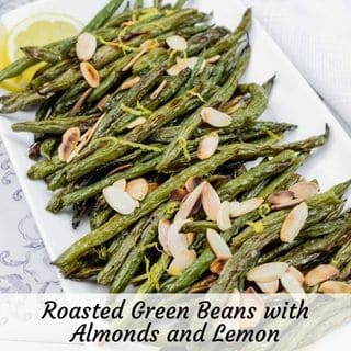 A plate of roasted green beans topped with sliced almonds and lemon wedges, served on a white rectangular dish.