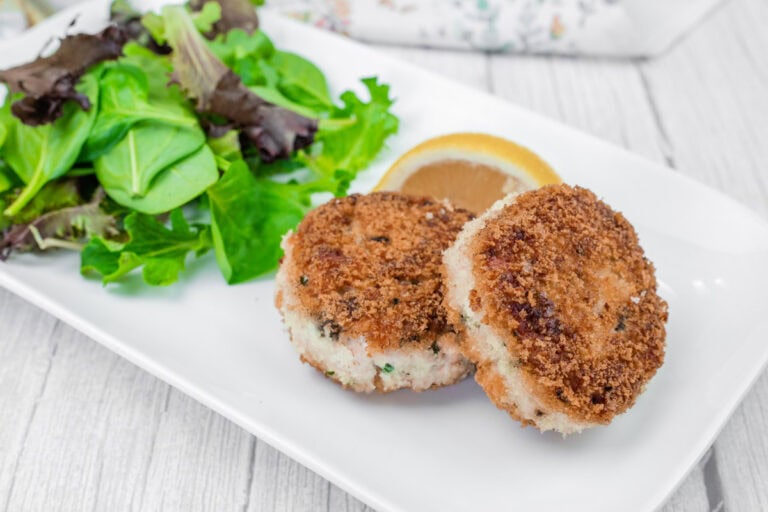 Two salmon cakes on a white plate with leafy greens on the side.
