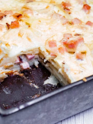 A rectangular pan of Scalloped Potatoes with Ham and Cheese, partially sliced, showing layers.