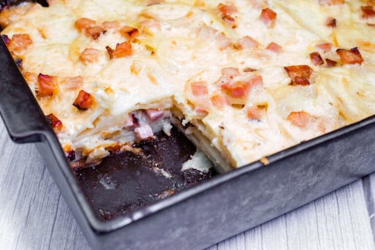 Rectangular pan of scalloped potatoes with ham and cheese, partially sliced to show layers.