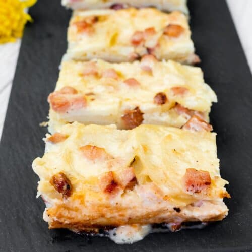 Four rectangular slices of Scalloped Potatoes with Ham and Cheese on a black slate.