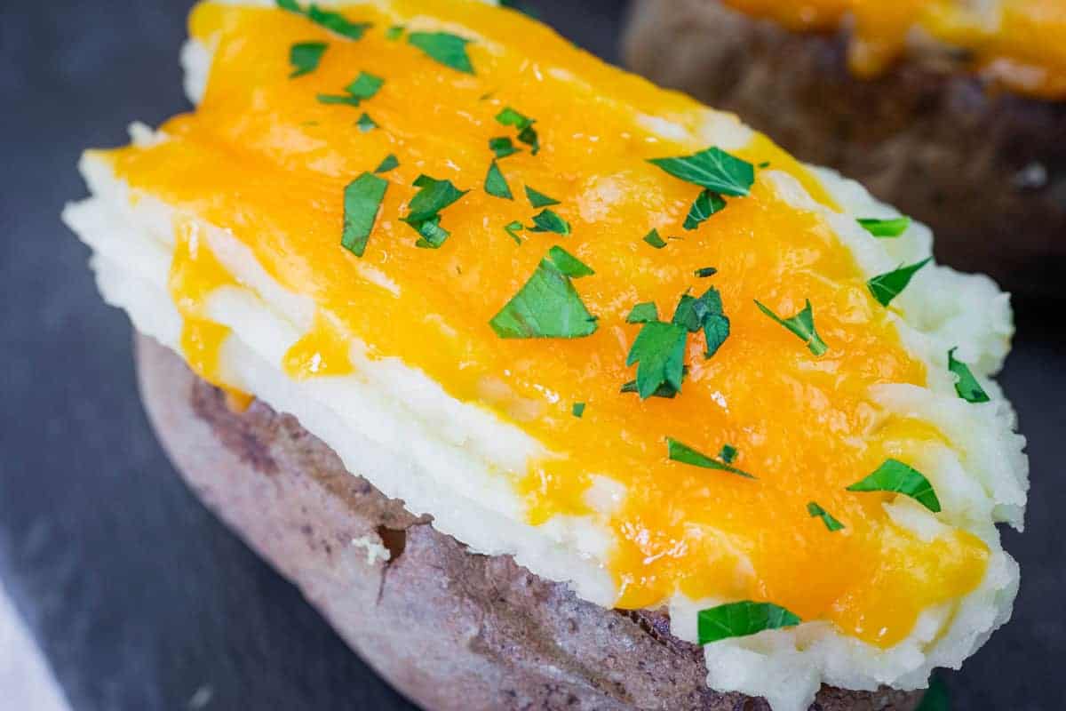 Close-up of Shepherd&rsquo;s Pie Baked Potatoes topped with melted cheddar cheese and chopped parsley.