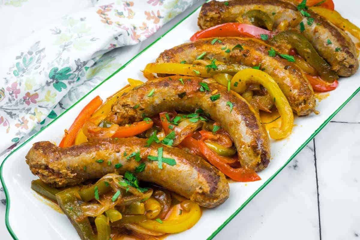 Five cooked Crock Pot Sausage and Peppers served on a white rectangular dish, garnished with chopped herbs.