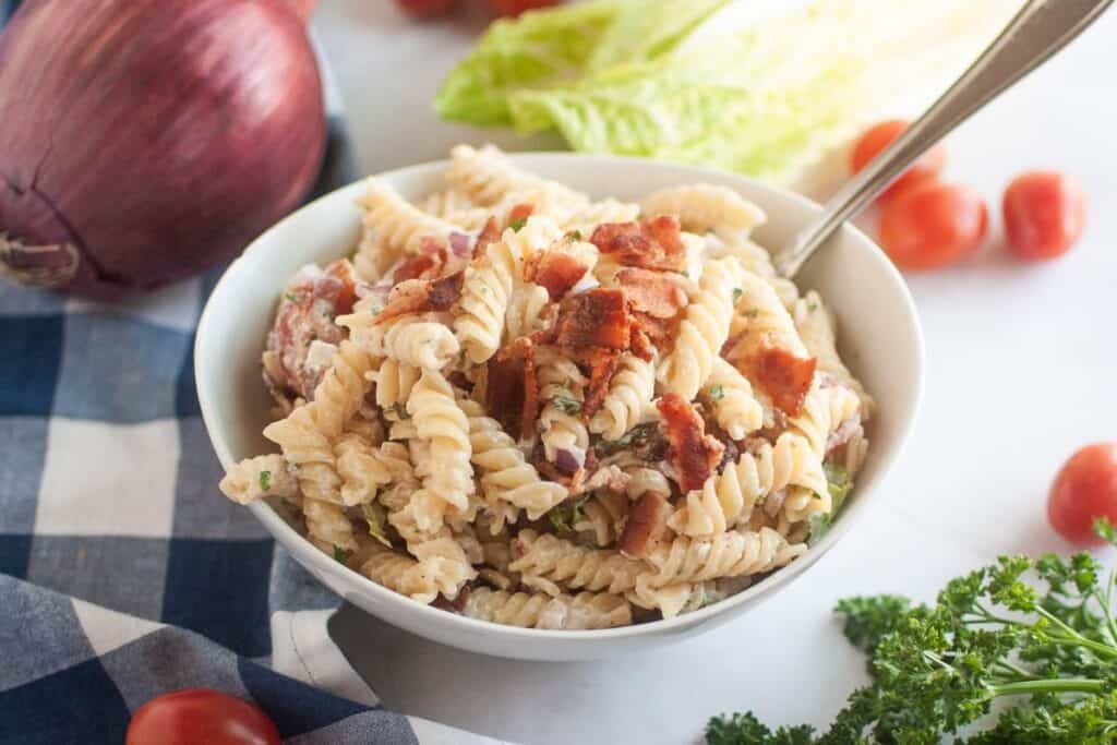 A white bowl filled with BLT pasta salad, featuring spiral pasta, creamy dressing, and pieces of bacon.