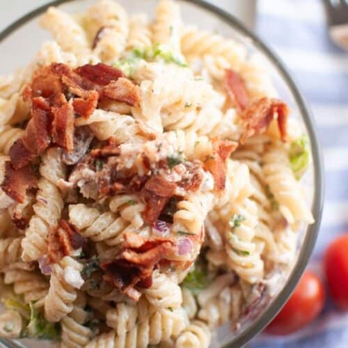Overhead shot of a glass bowl filled with BLT pasta salad, featuring spiral pasta, creamy dressing, and pieces of bacon.