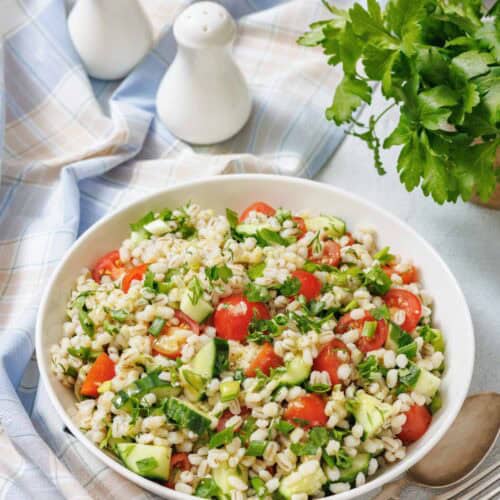 Bowl of barley salad with cucumber, cherry tomatoes, herbs, and green onions.