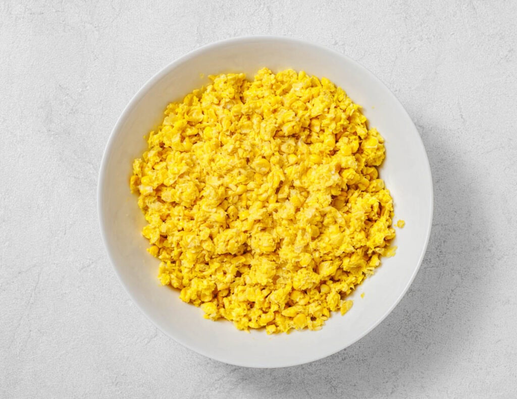 A white bowl filled with corn mixture sits on a light gray surface.