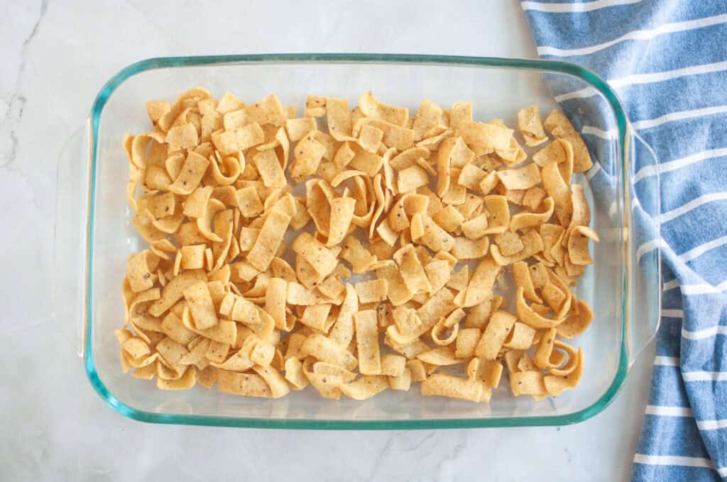 Overhead shot of corn chips arranged in a clear glass baking dish, with a blue striped cloth beside it.