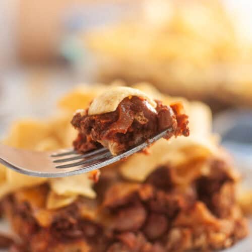 A fork lifts a bite of frito pie, with a larger portion of the pie visible in the background.