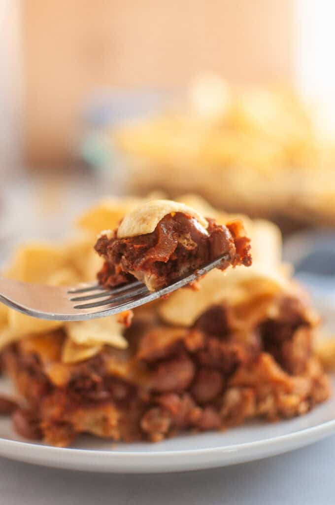 A fork lifts a bite of frito pie, with a larger portion of the pie visible in the background.