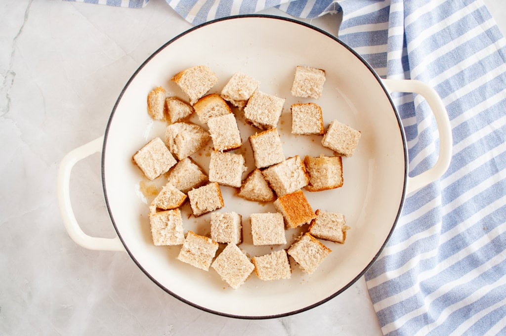 Overhead shot of bread cubes in a white pan, with a striped cloth.