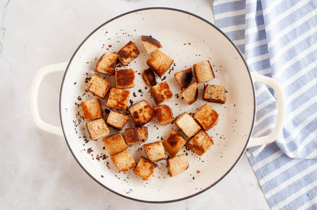 Overhead shot of toasted croutons in a white pan, with a striped cloth.