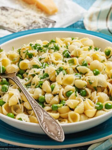 A bowl of pasta and peas with a fork, grater, and cheese on the side.