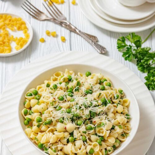 A white bowl filled with pasta and peas, garnished with cheese and parsley.