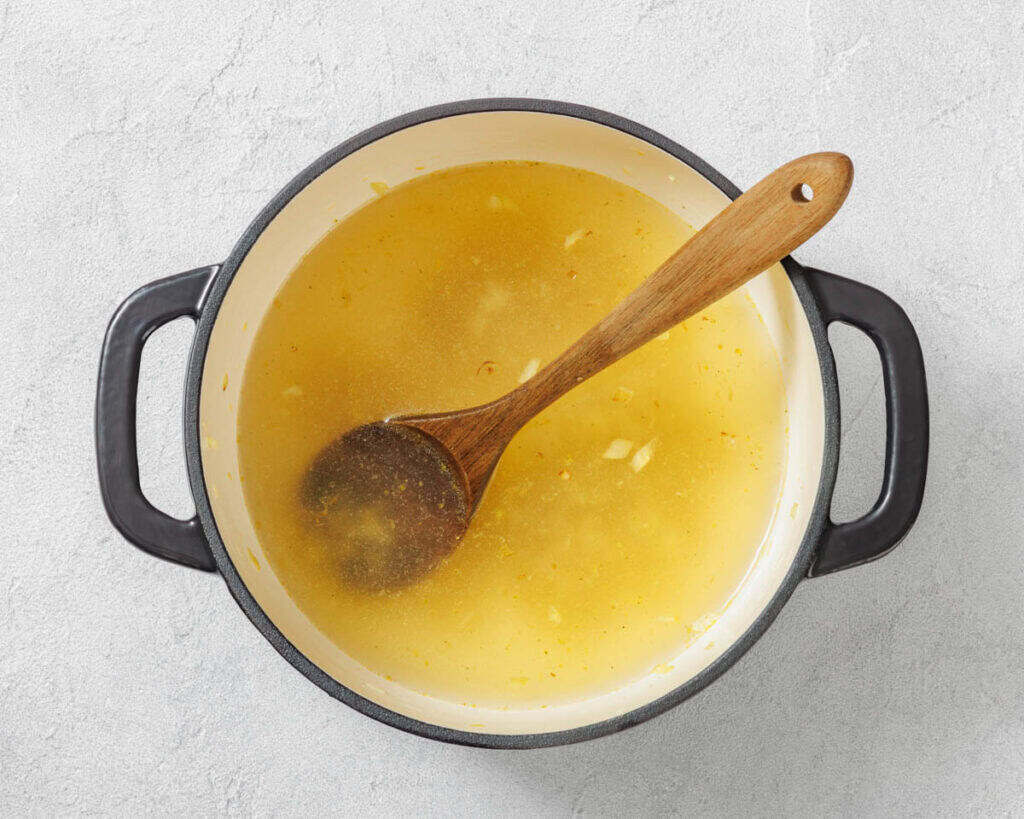 Overhead shot of yellow broth in a black pot with a wooden spoon.