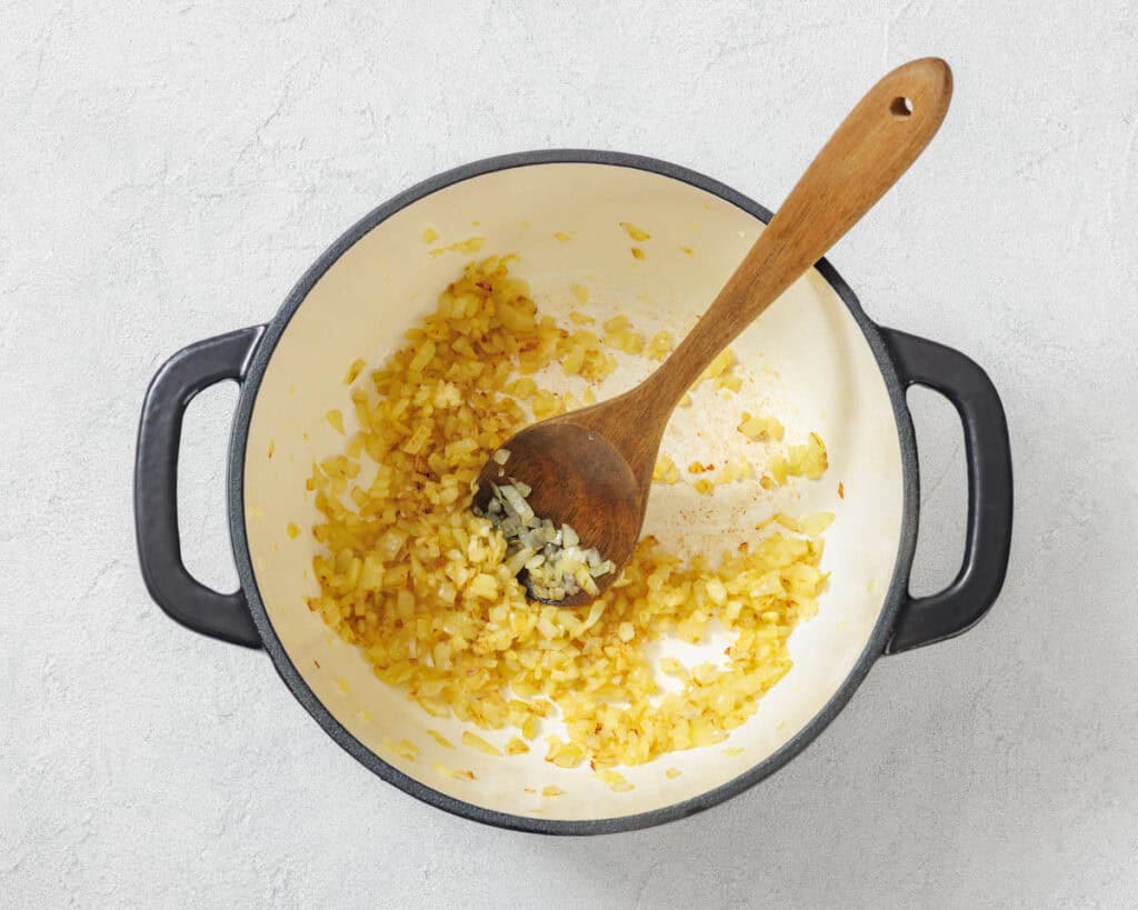 Overhead shot of saut&eacute;ed onions in a black pot with a wooden spoon.