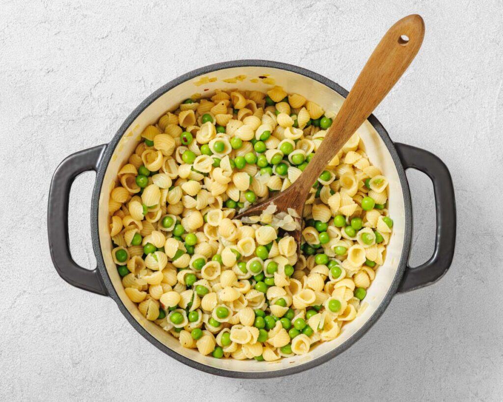 Overhead shot of pasta and peas in a black pot with a wooden spoon.