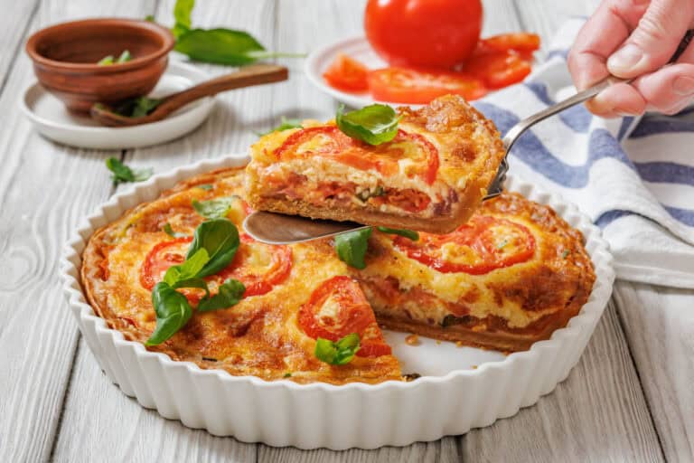 A slice of tomato pie being lifted with a serving utensil from a white fluted dish.
