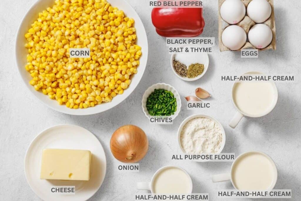 Ingredients for a recipe are arranged on a white surface, including corn, red bell pepper, eggs, cheese, onion, chives, garlic, flour, seasonings, and half-and-half cream.