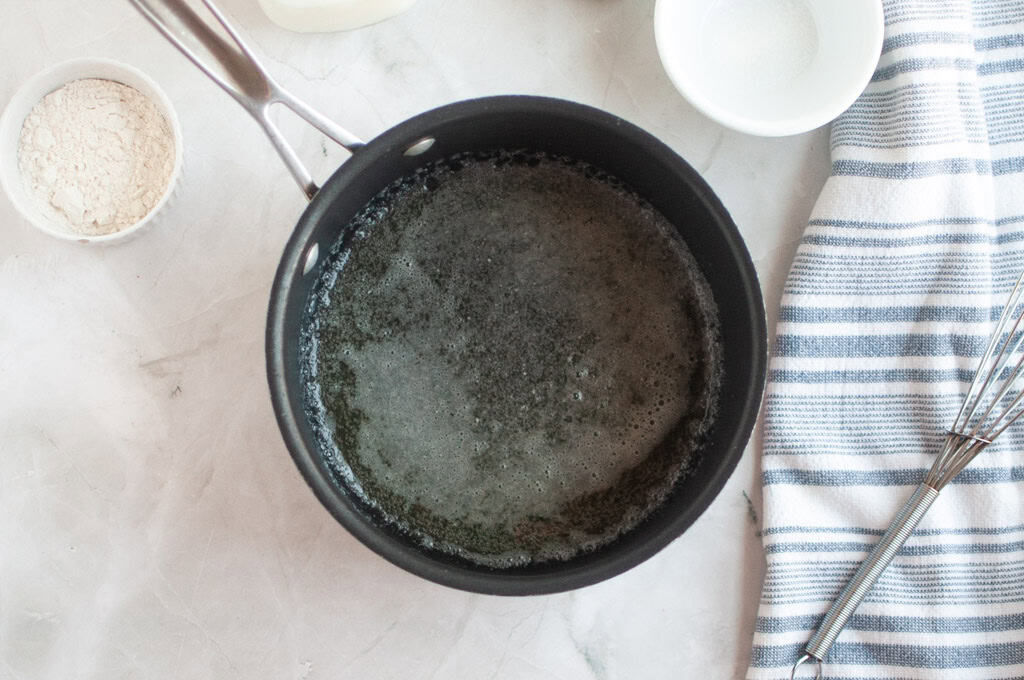 Overhead shot of melted butter bubbling in a black saucepan, with other ingredients nearby.