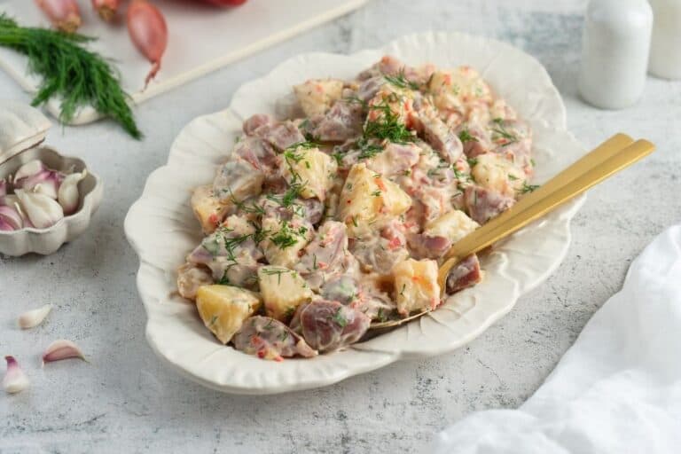 Serving dish filled with classic red potato salad with pickles.