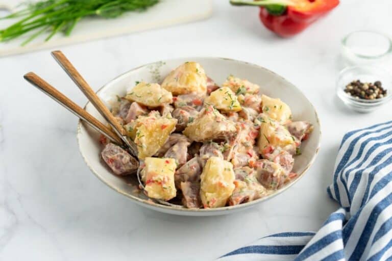 Creamy red potato salad with pickles served in a bowl.
