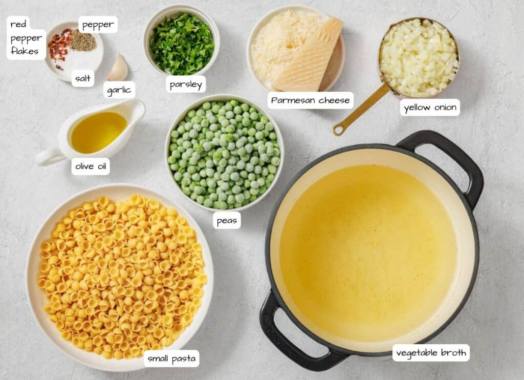 Overhead shot of pea pasta ingredients, including pasta, peas, cheese, onions, spices, and oil, arranged on a light surface with labels for each ingredient.
