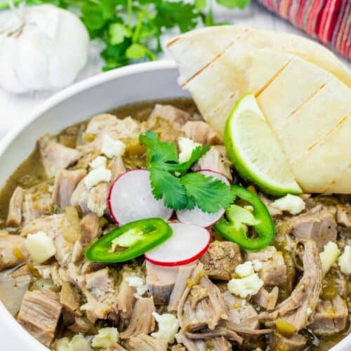 Bowl of slow cooker pork chile verde with toppings on a white wooden table.