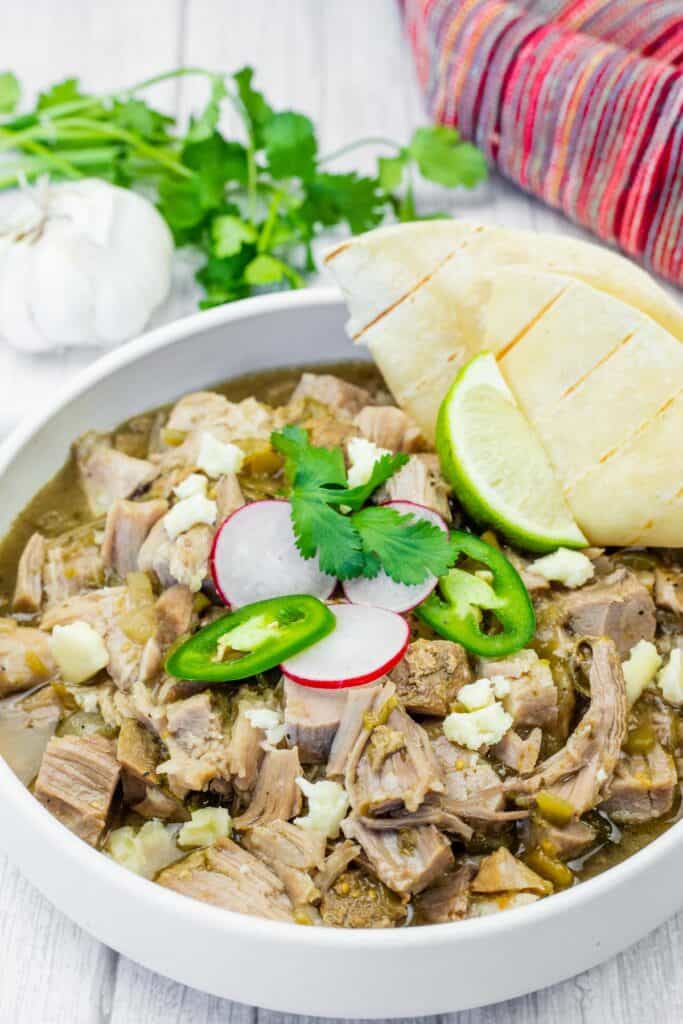 Bowl of Slow Cooker Pork Chile Verde with toppings on a white wooden table.