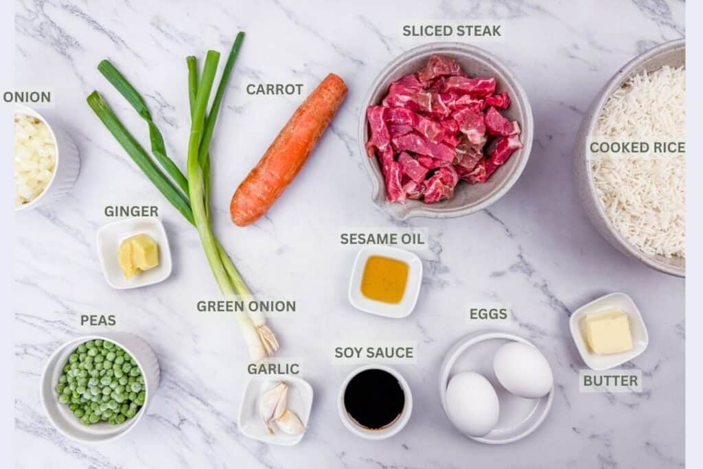 Rice, sliced steak, carrot, oil, eggs, butter, soy sauce, garlic, peeled ginger, sliced onion, green onion, and peas on a marbled white-gray surface with labels.