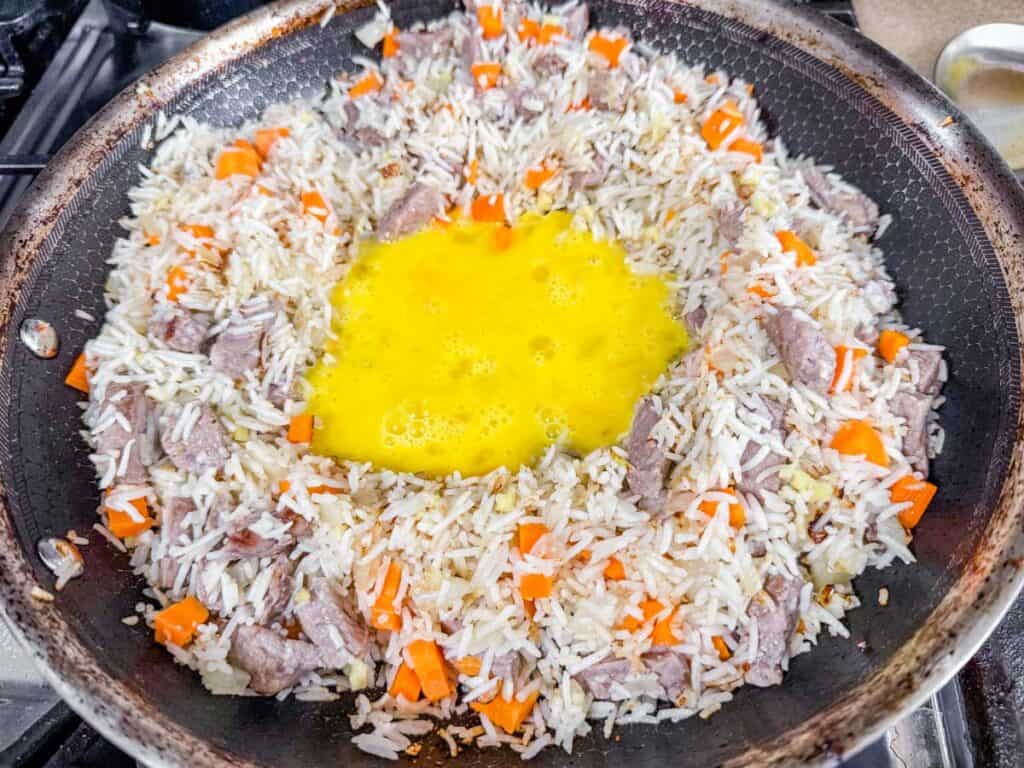Sauted rice with carrots and raw egg in the middle of a skillet pan.