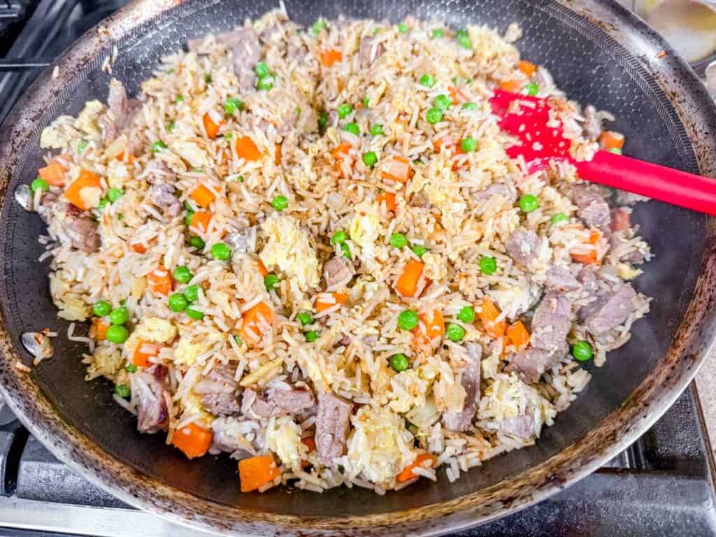 cooked steak fried rice in a pan with red spatula.