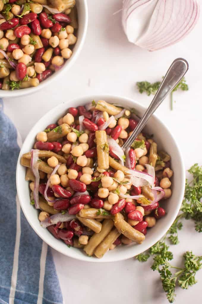 Bowl of Grandma&rsquo;s Three Bean Salad featuring kidney beans, chickpeas, and green beans, garnished with thinly sliced red onions and fresh parsley.