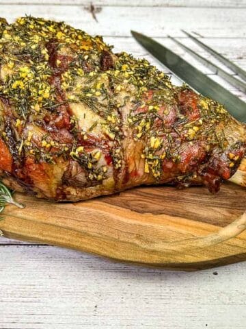Whole cooked leg of lamb on a board with a knife.