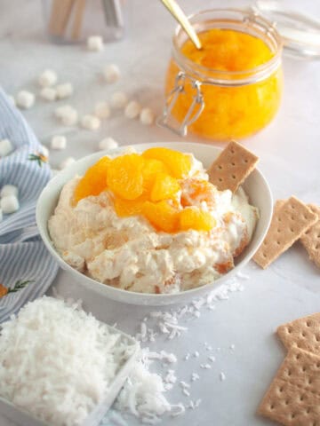 Overhead shot of a white bowl filled with creamy Orange Fluff Salad, topped with mandarin oranges and served with graham crackers.