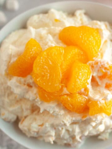 Overhead shot of a white bowl filled with creamy orange fluff salad, topped with mandarin oranges and served with graham crackers.