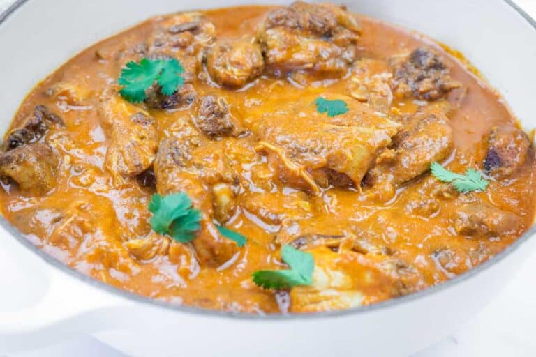 A white pot filled with Slow-Cooker Chicken Tikka Masala, garnished with a few cilantro leaves.