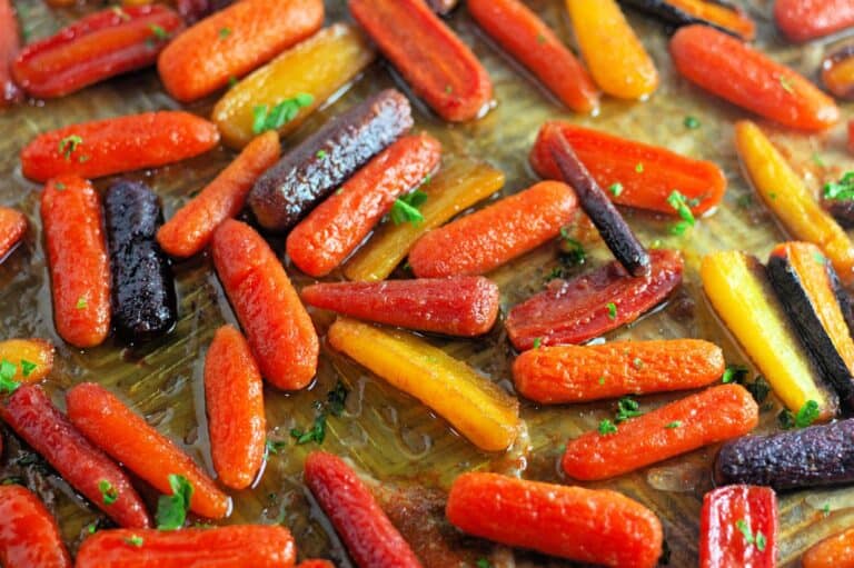A close-up of roasted multicolored baby carrots garnished with chopped herbs on a baking sheet.