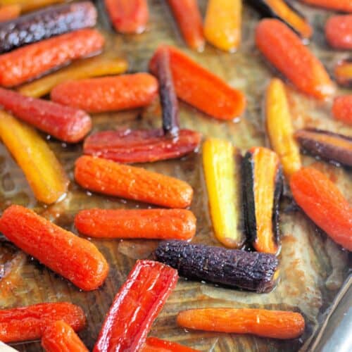 Rainbow baby carrots roasted on a parchment-lined baking sheet.