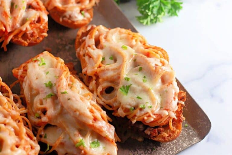 Sliced bread topped with spaghetti, meat sauce, and melted cheese, garnished with chopped parsley, arranged on a baking sheet.