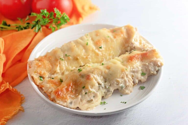 Two baked, cheese-covered cannelloni stuffed with a creamy filling are served on a white plate, garnished with chopped herbs.
