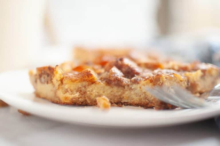 A close-up of a partially eaten piece of Cinnamon Roll Casserole on a white plate, with a fork resting beside it.