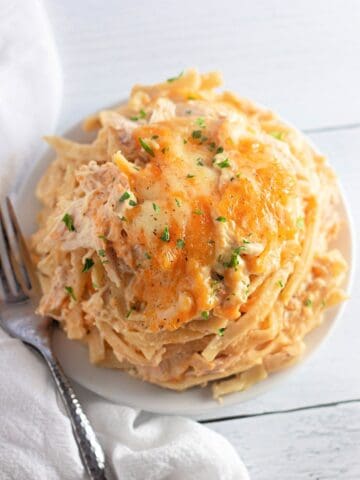 A plate of creamy pasta topped with melted cheese and chopped herbs, with a fork and a white napkin beside it.